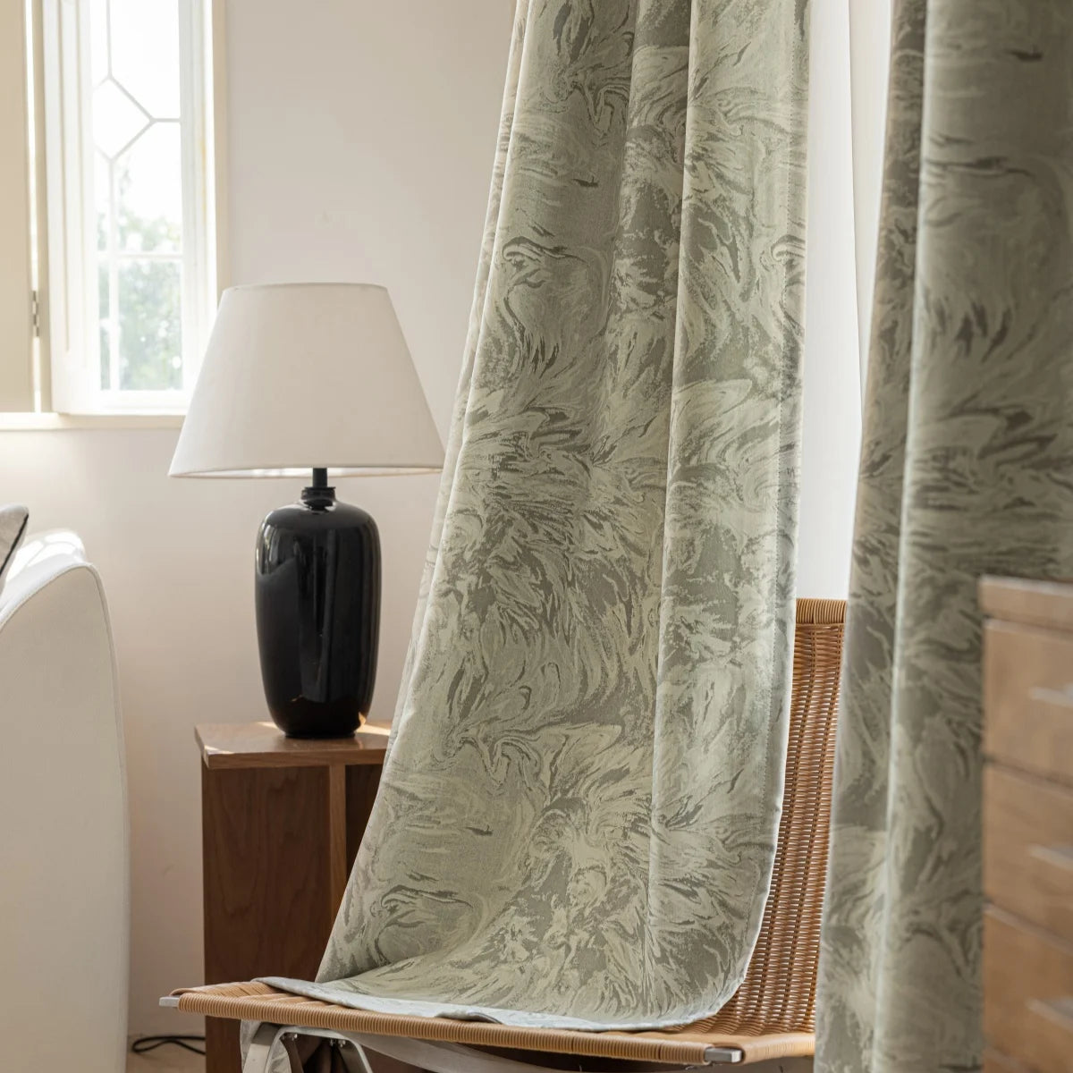 Sage jacquard curtain falling onto rattan chair in afternoon light